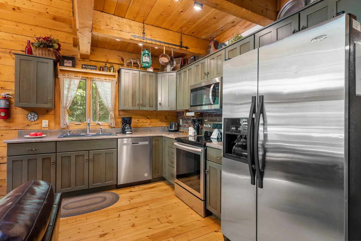 A close-up of the kitchen area with stainless steel appliances, wooden cabinets, a central island, and a window letting in natural light. It feels welcoming and ready for joyful meal prep and family recipes.