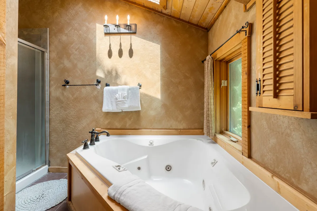 A serene bathroom with a jacuzzi tub surrounded by wooden accents and filled with natural light from a window. The ambiance is calm and luxurious, perfect for unwinding after a long day.