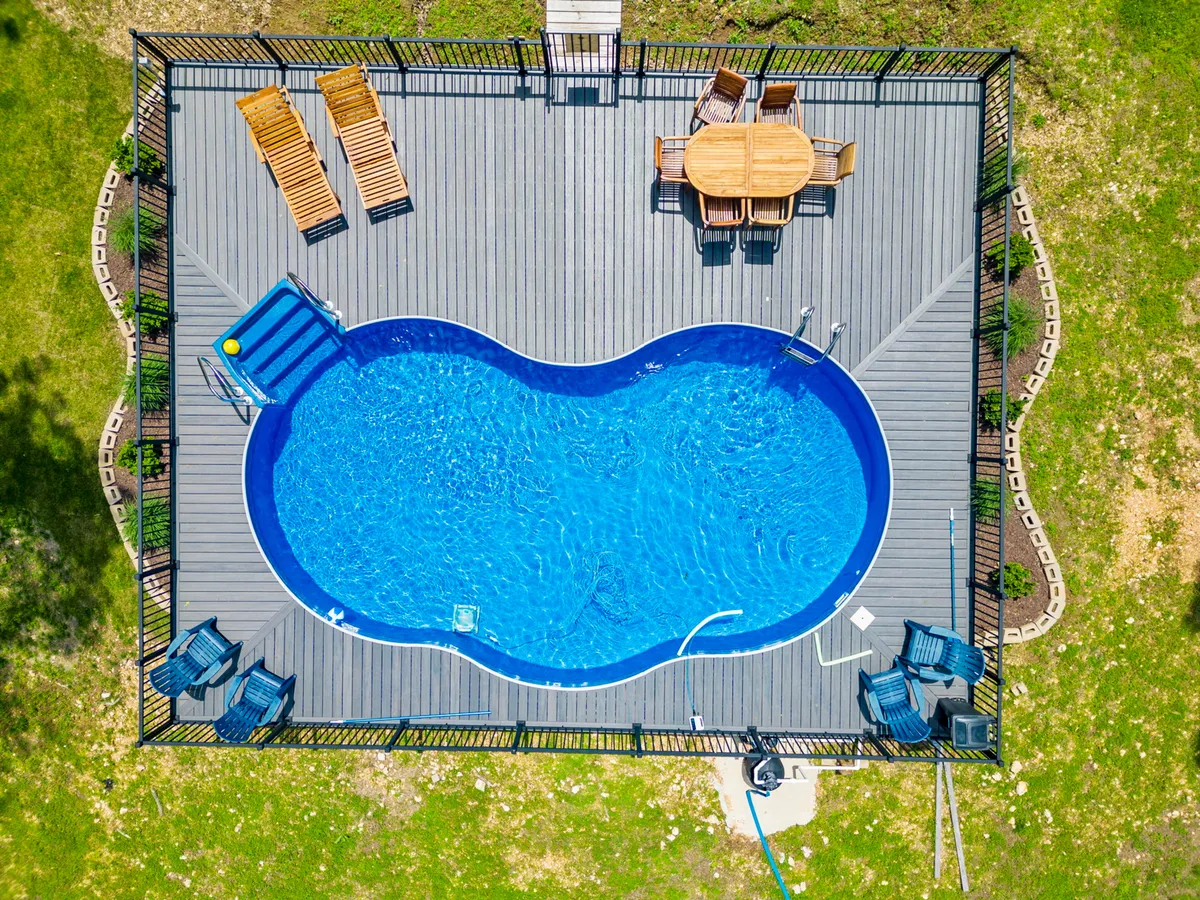 An inviting outdoor area with a swimming pool, sun loungers, and an outdoor dining table set on a spacious deck. Surrounded by trees, the space offers scenic views and is suited to sunset dinners, afternoon lounging, and social outdoor meals.