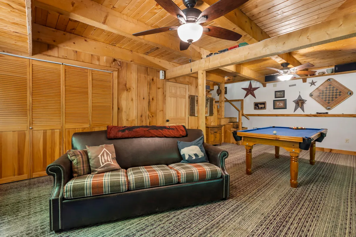 A cozy interior scene with a plaid sofa, pool table, exposed wooden ceiling beams, and playful wall art, evoking a sense of warmth and togetherness during friendly game nights or casual hangouts.