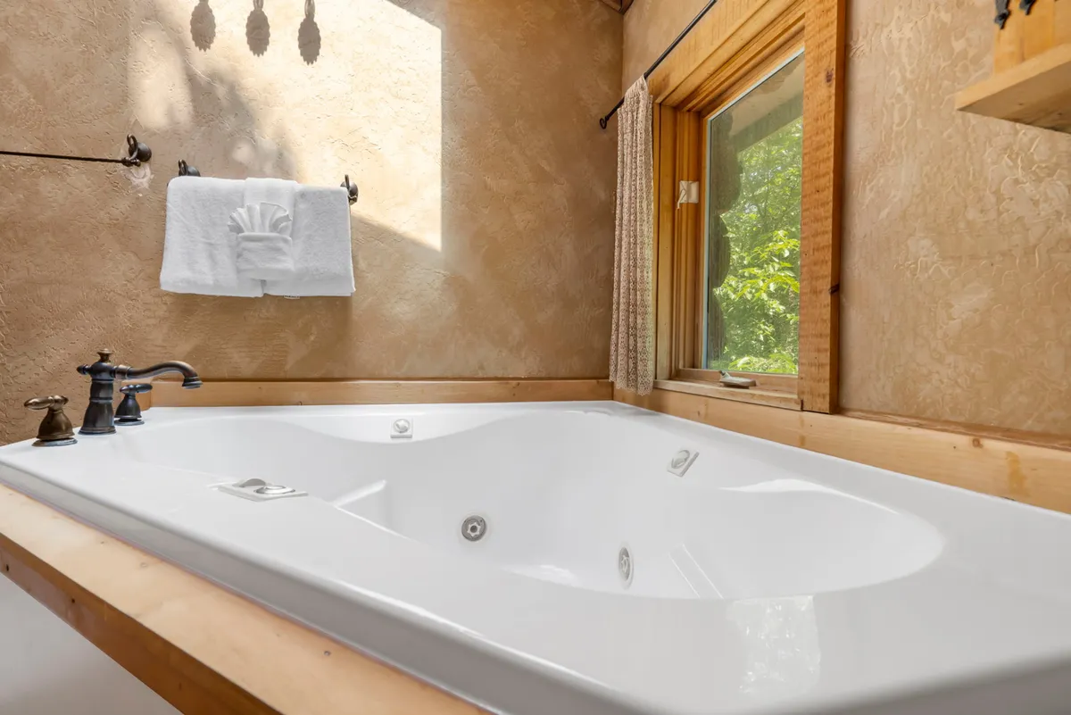 A tranquil bathroom scene with a jacuzzi tub positioned near a window letting in ample natural light. A towel hangs on a nearby rack, suggesting comfort and relaxation.