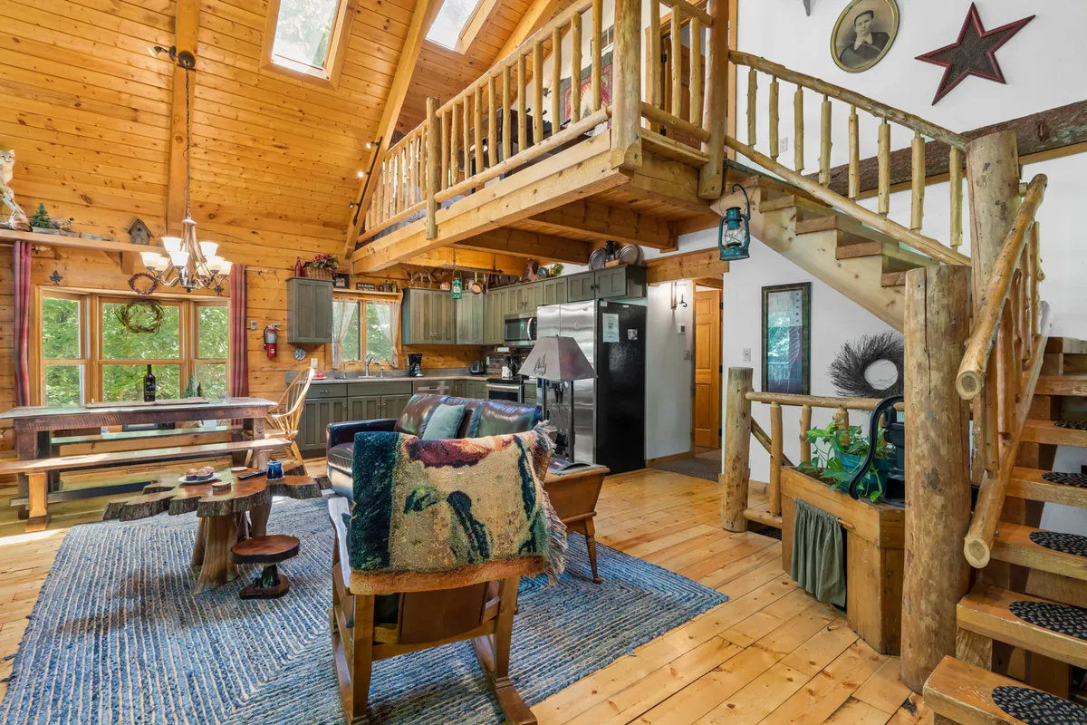 A wide view of the main level’s open-concept space, highlighting the wooden beams, kitchen area, dining table, and large windows that flood the interior with light. The layout invites group activities and shared meals.