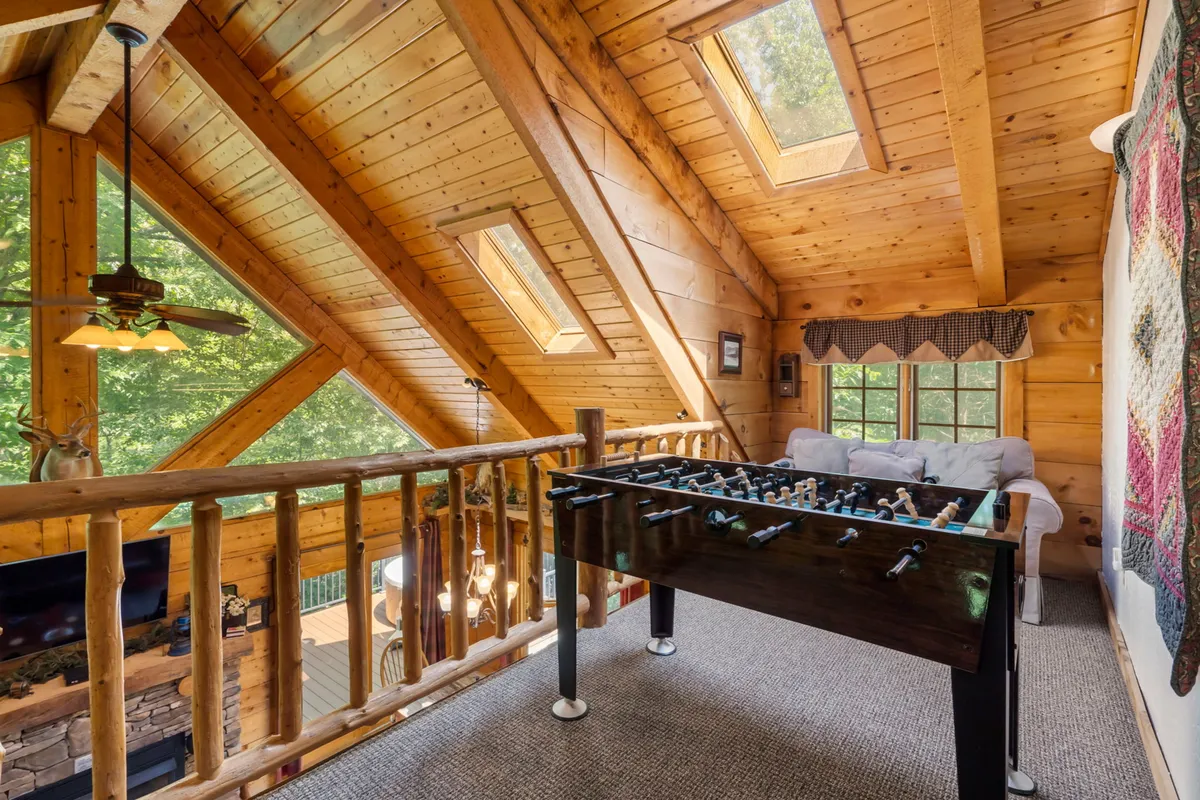 A bright upstairs loft area with a foosball table, wooden beams, skylights flooding the space with natural light, and a comfortable seating area ideal for casual relaxation or friendly competition.